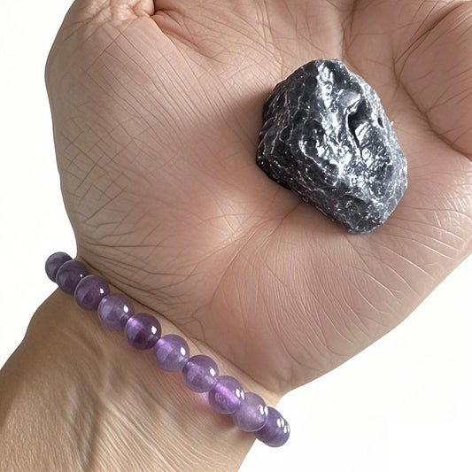 A person wearing a amethyst bracelet, holding a rough amethyst crystal in hand.