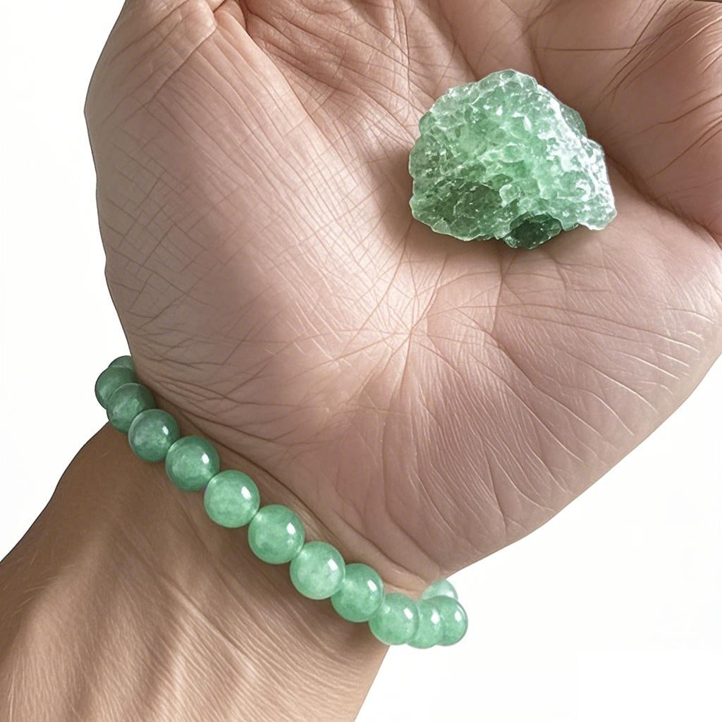 A person wearing a green aventurine bracelet, holding a rough green aventurine crystal in hand.