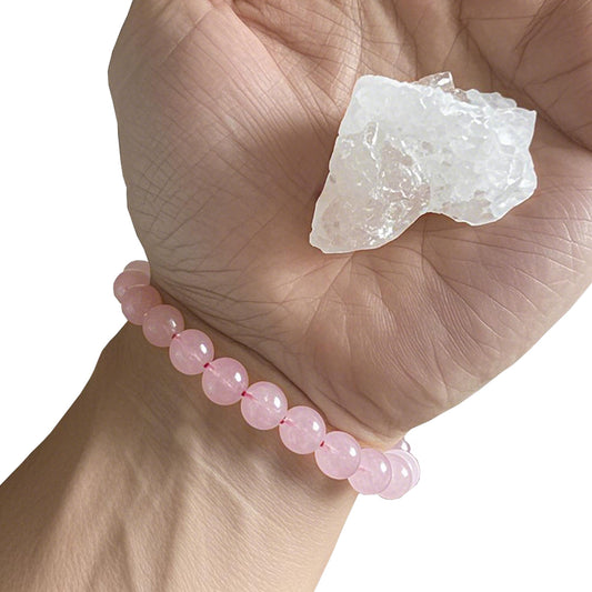 A person wearing a rose quartz bracelet, holding a rough rose quartz crystal in hand.